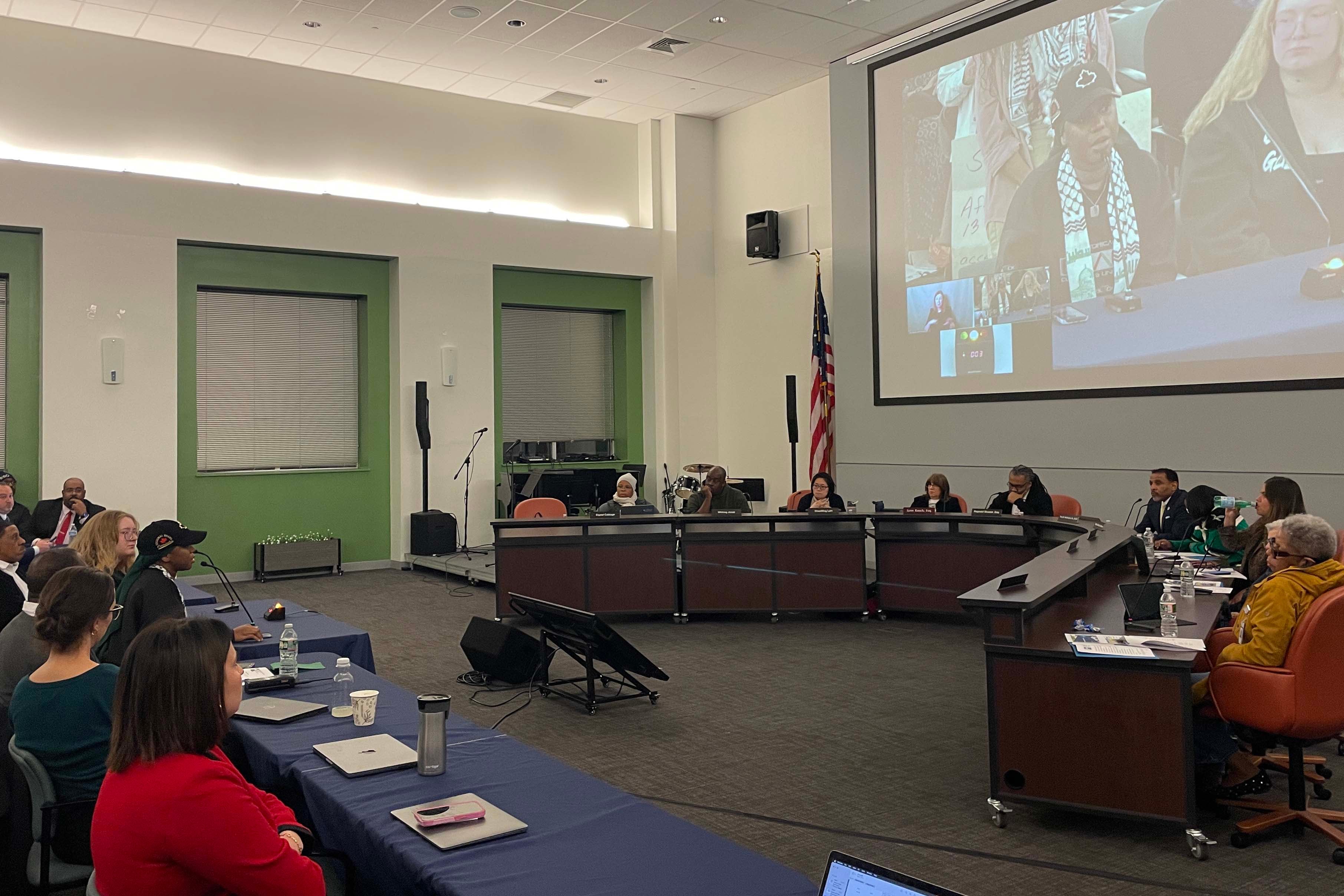 A photograph of two rows of people sitting in a large conference room facing each other during a meeting.
