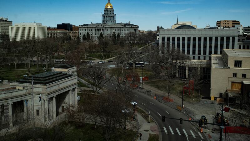 The Colorado State Capitol is seen from some distance, surrounded by other buildings, its dome glowing slightly.