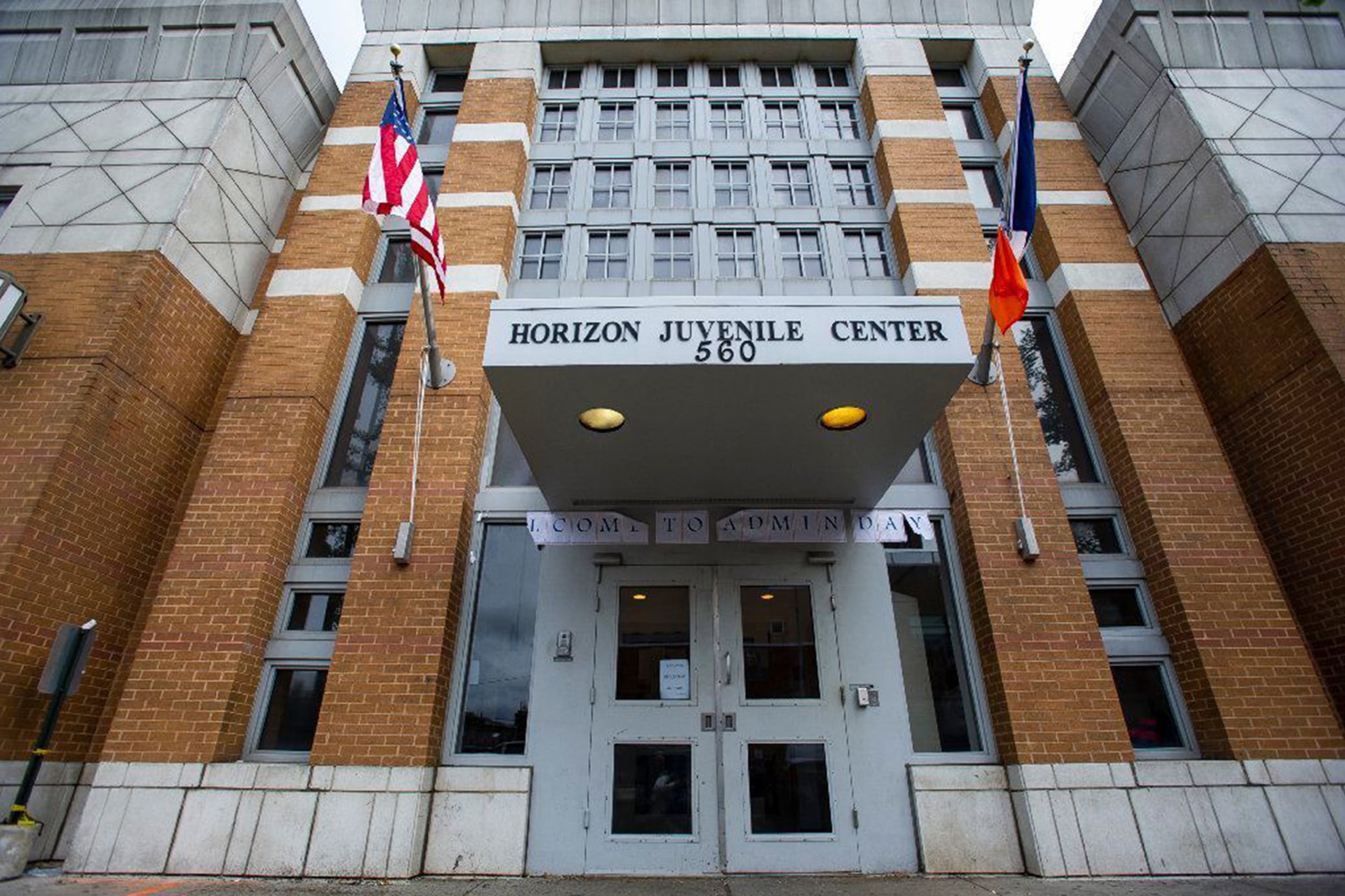 A photograph of the outside of a large stone building with two flags on each side of the entrance that reads "Horizon Juvenile Center."