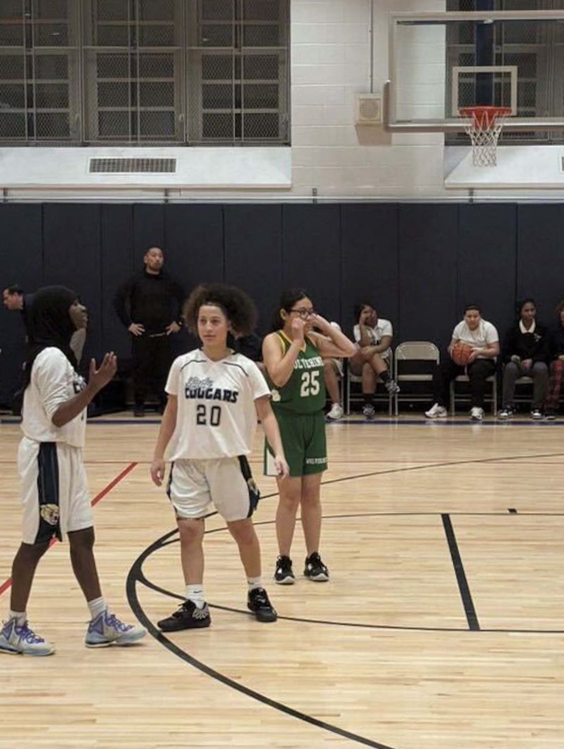 Three high school students wearing basketball uniforms play during a game on a basketball court.