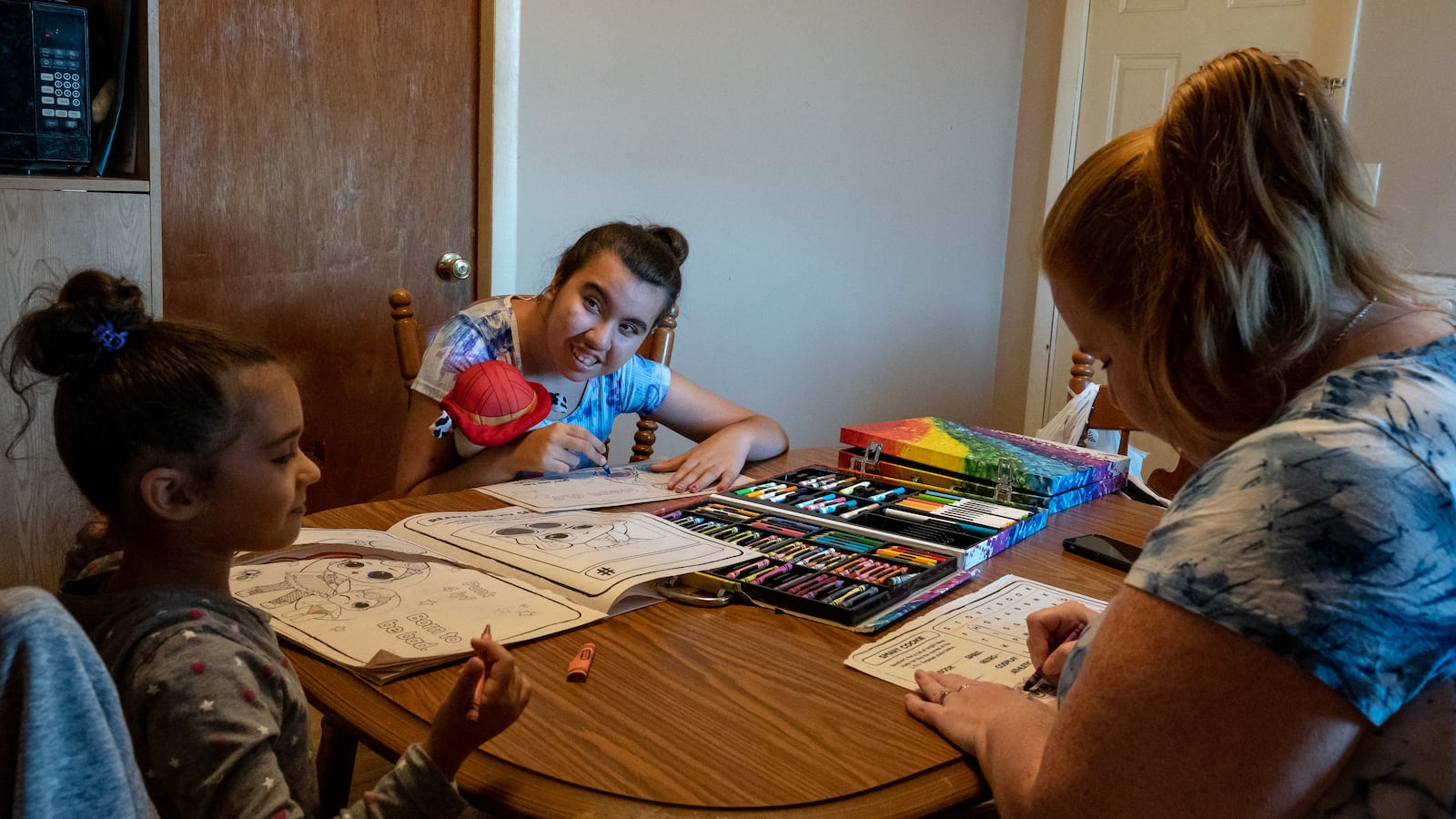 Two girls and a woman color in coloring books together at a dining room table.