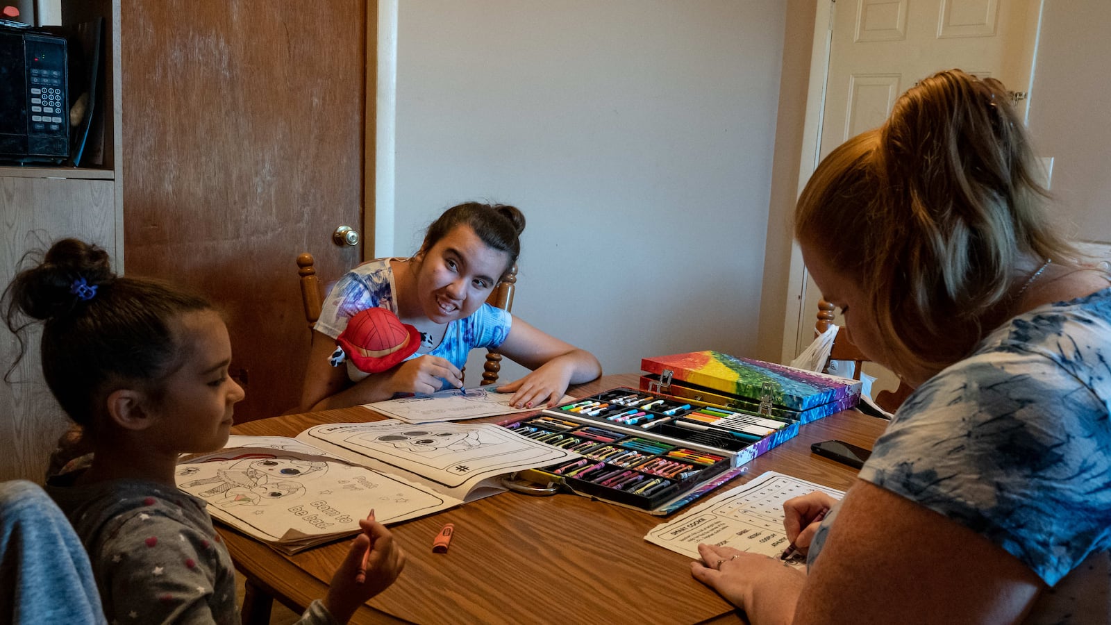 Two girls and a woman color in coloring books together at a dining room table.