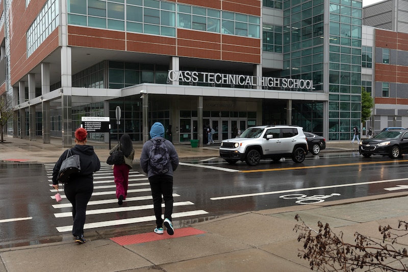 People cross the street in front of a school.