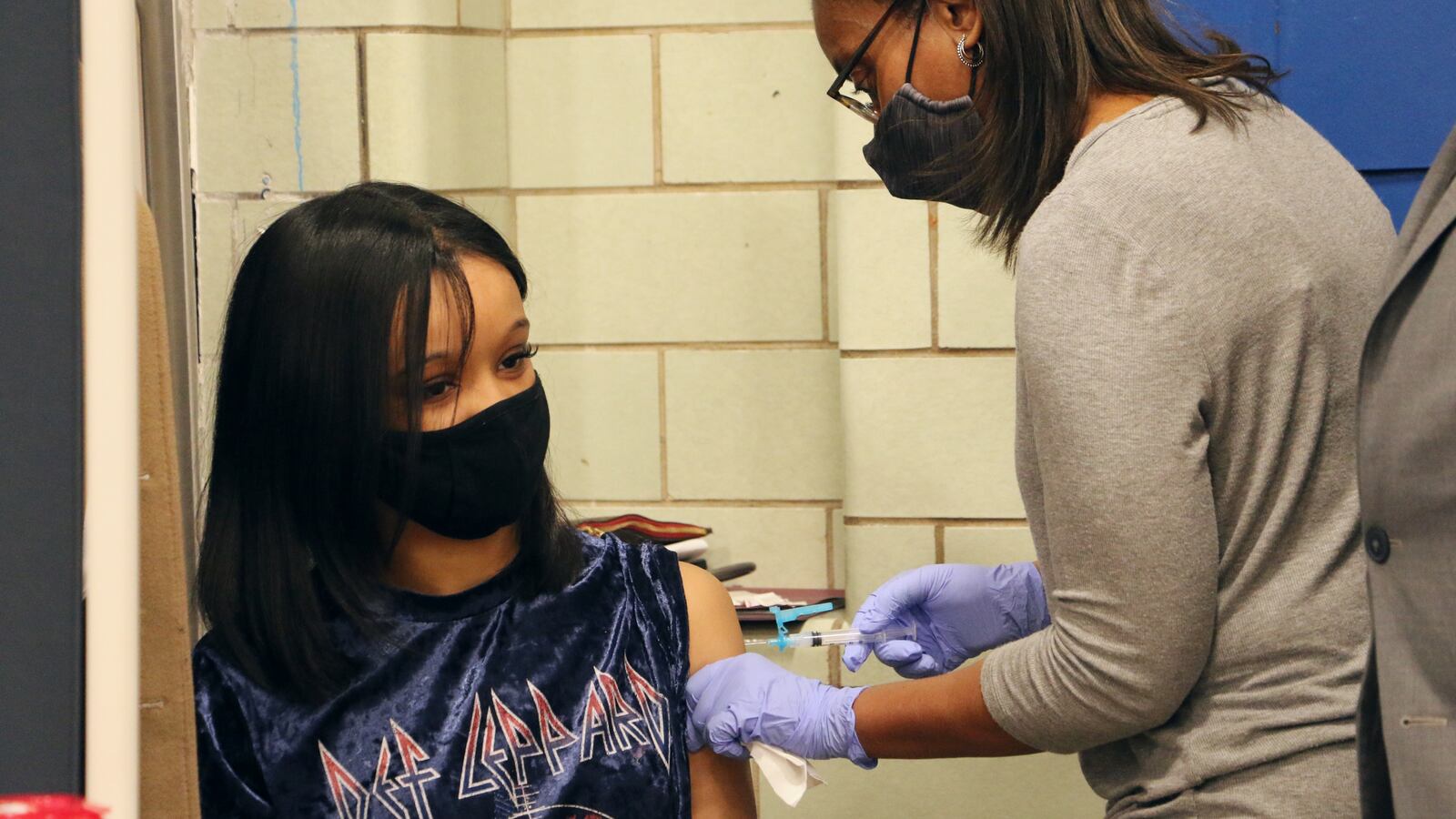 A young woman in a Def Leppard shirt receives a dose of a COVID vaccine.