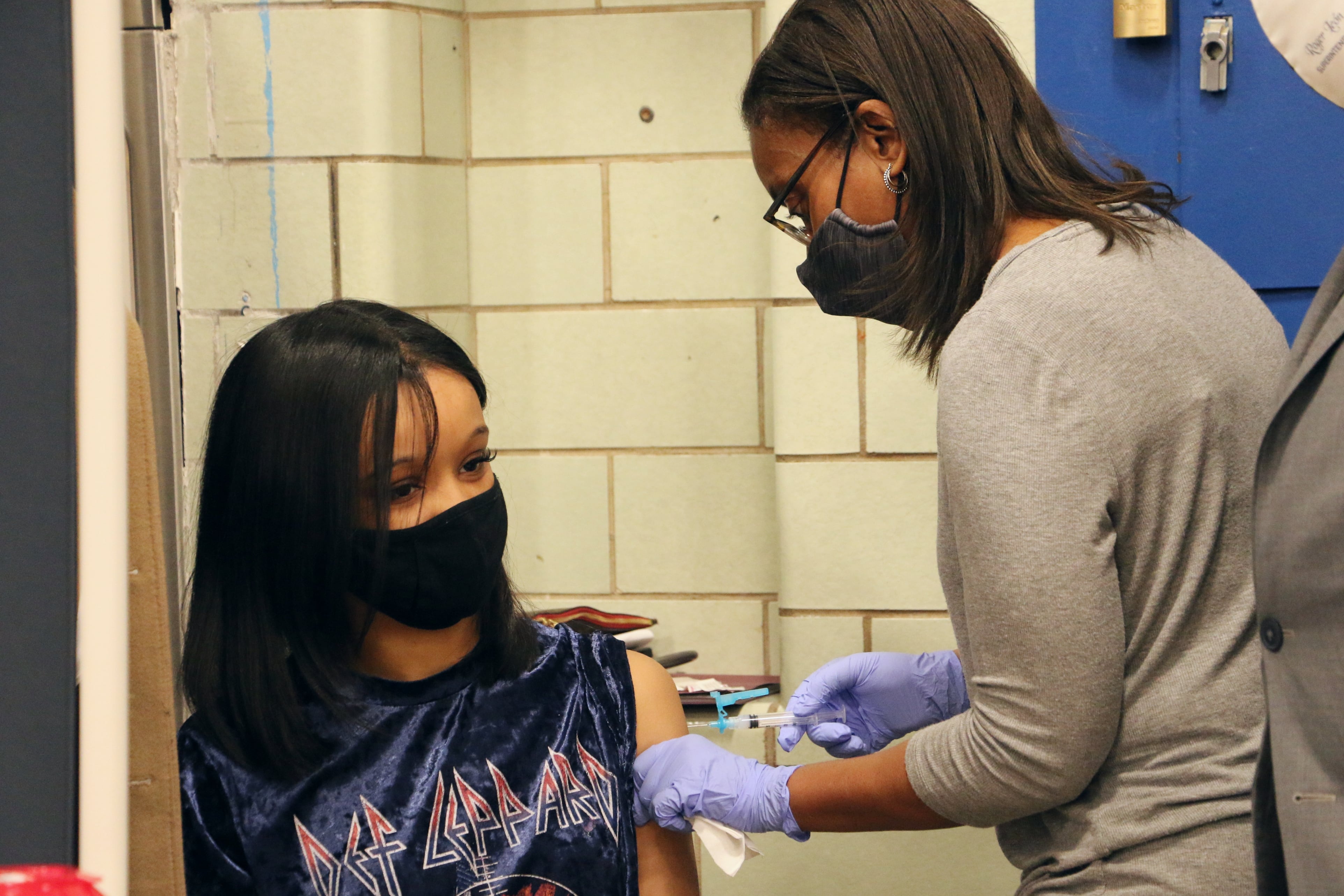 A young woman in a Def Leppard shirt receives a dose of a COVID vaccine.