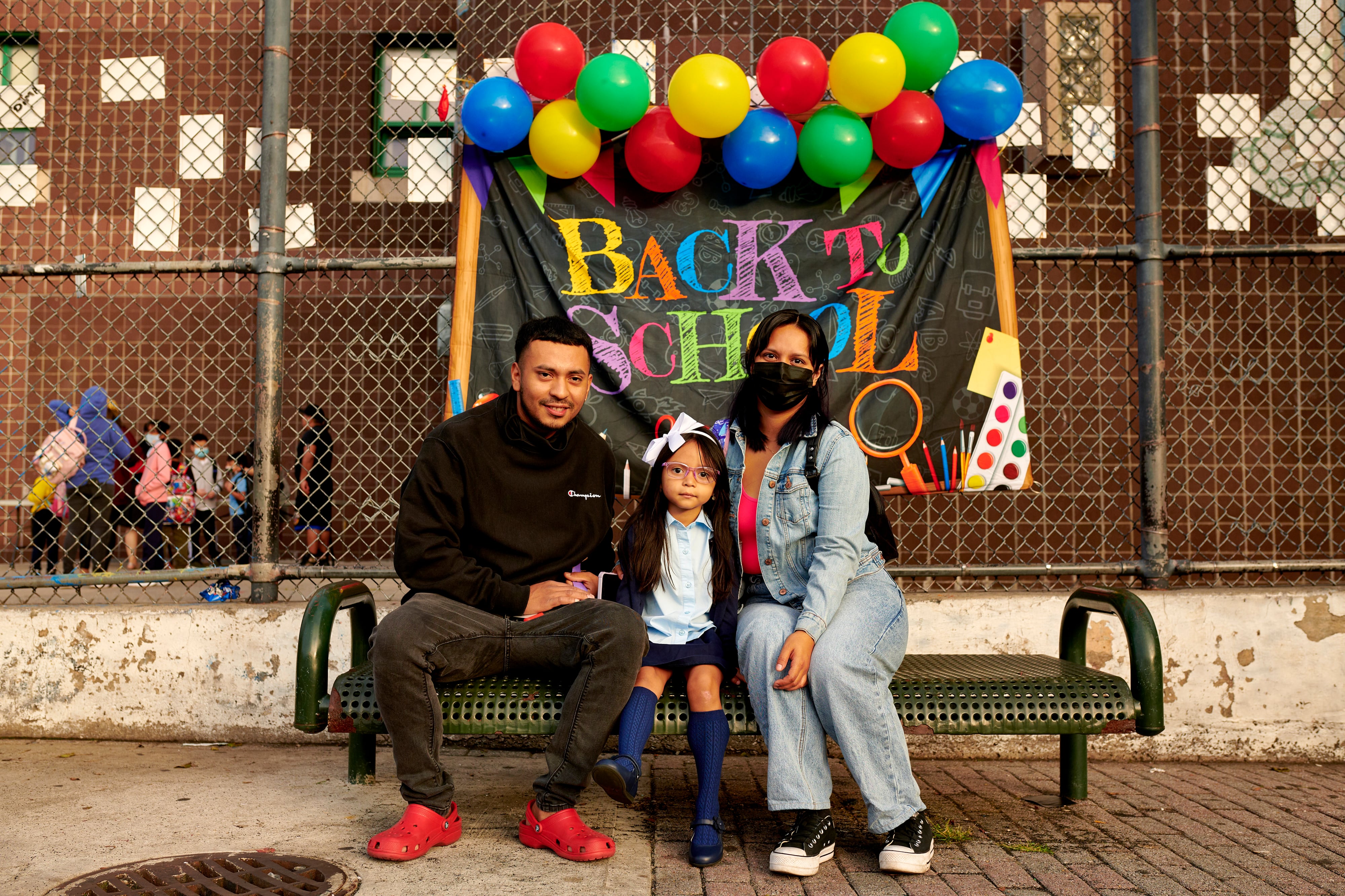 Two parents pose with their daughter for a portrait in front of a banner that reads, “Back to School.”