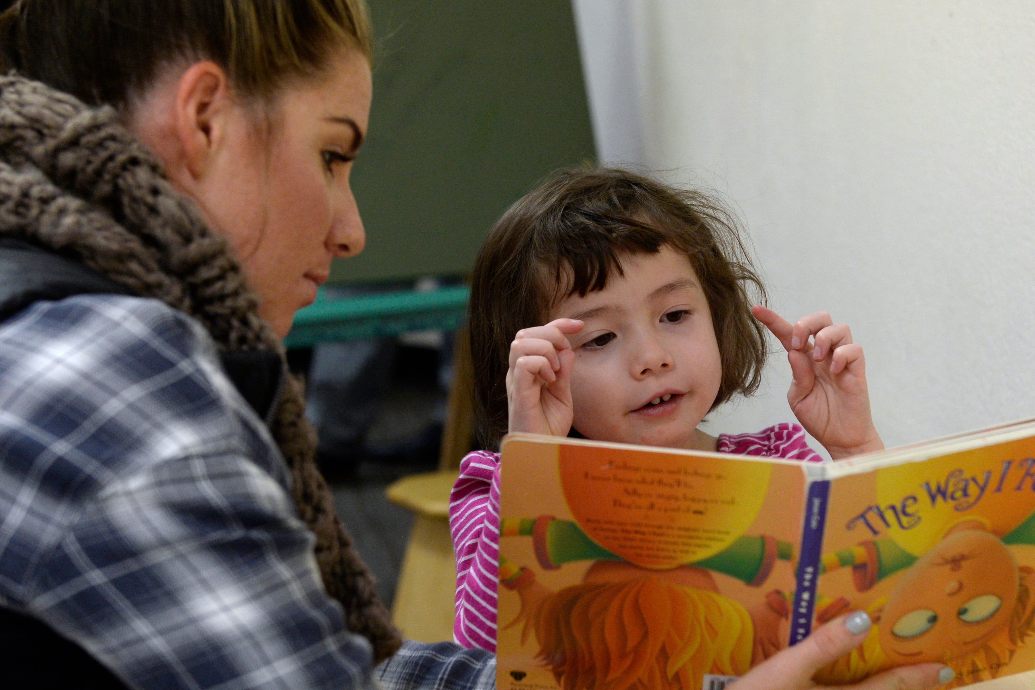 A photograph of a teacher reading a book to an elementary school-age kid.