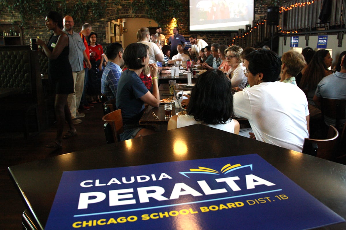 A blue sign rests on a table in front of a crowd of people.