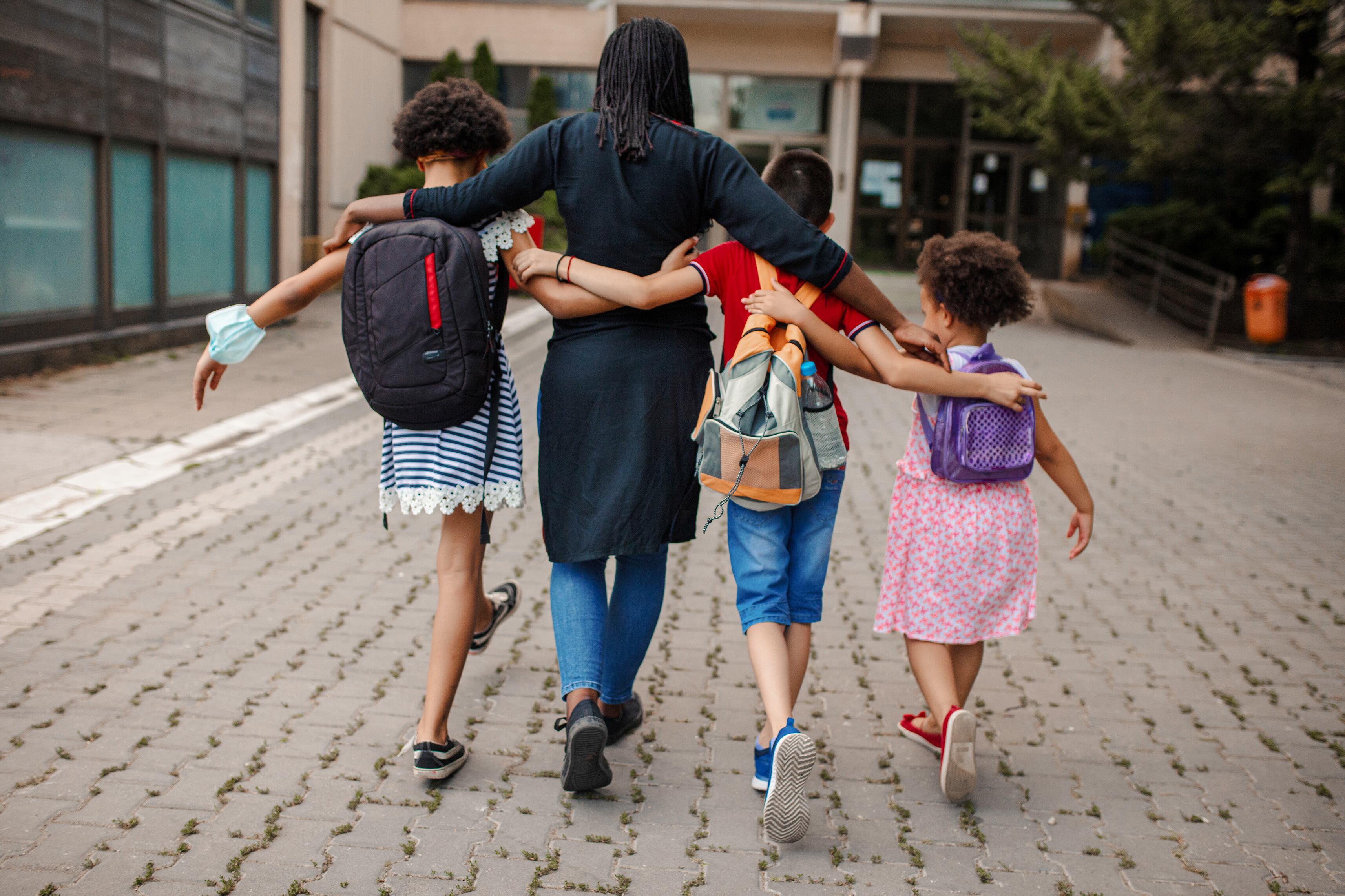 Three students wearing backpacks and a woman walking arm in arm away from the camera.