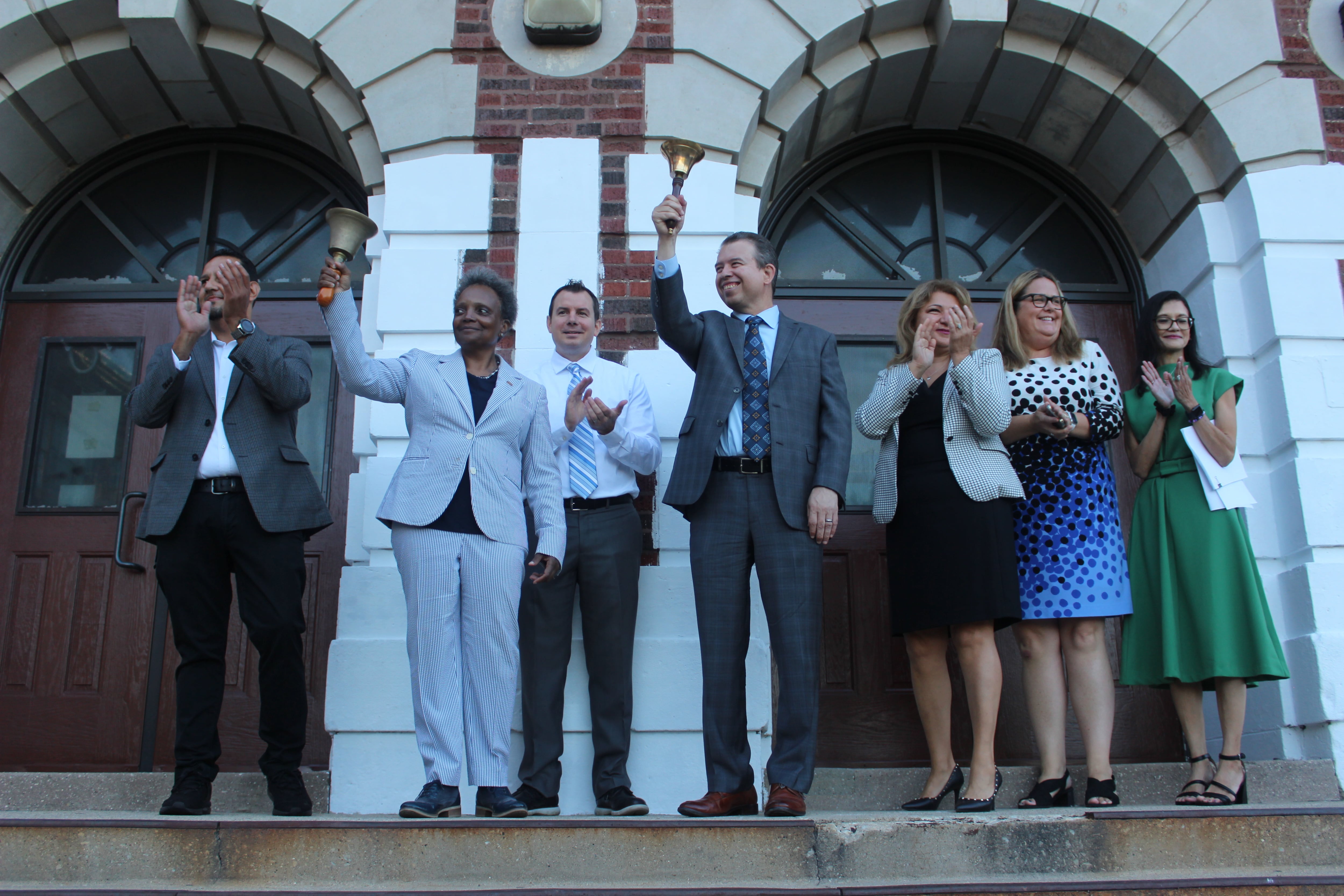 A group of men and women stand in front of a an elementary school on the first day of the new school year.