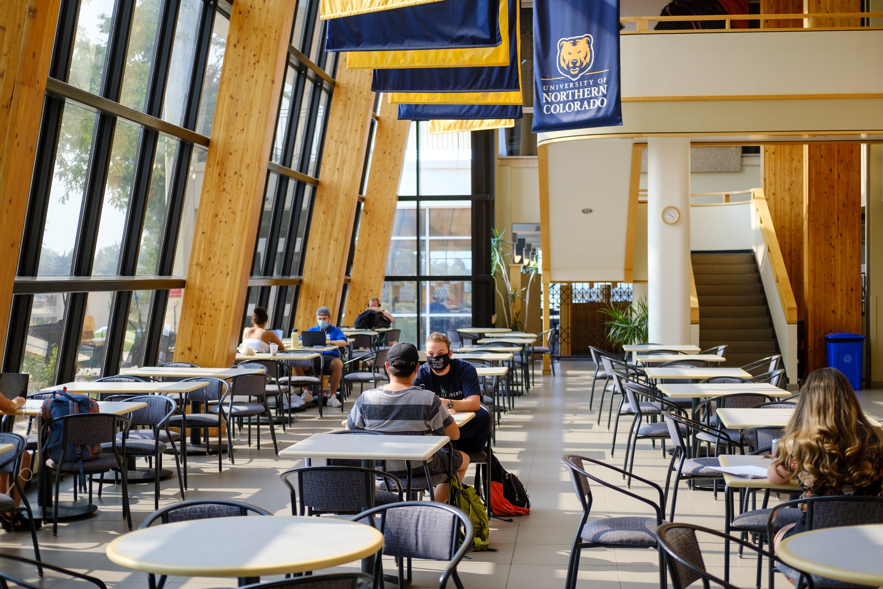 A room with floor-to-ceiling windows and students scattered at tables and chairs