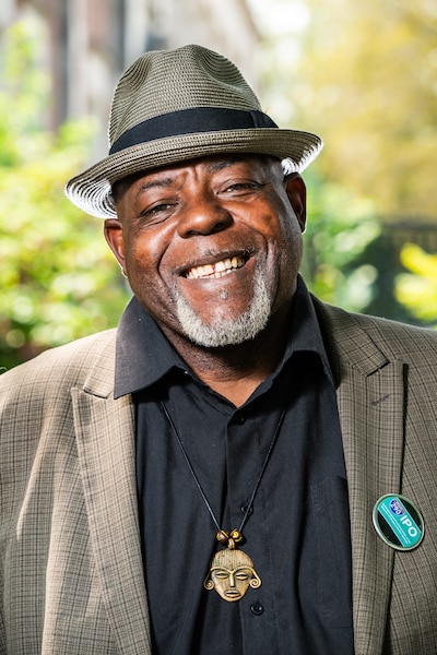 A man in a gray jacket, black shirt and hat.
