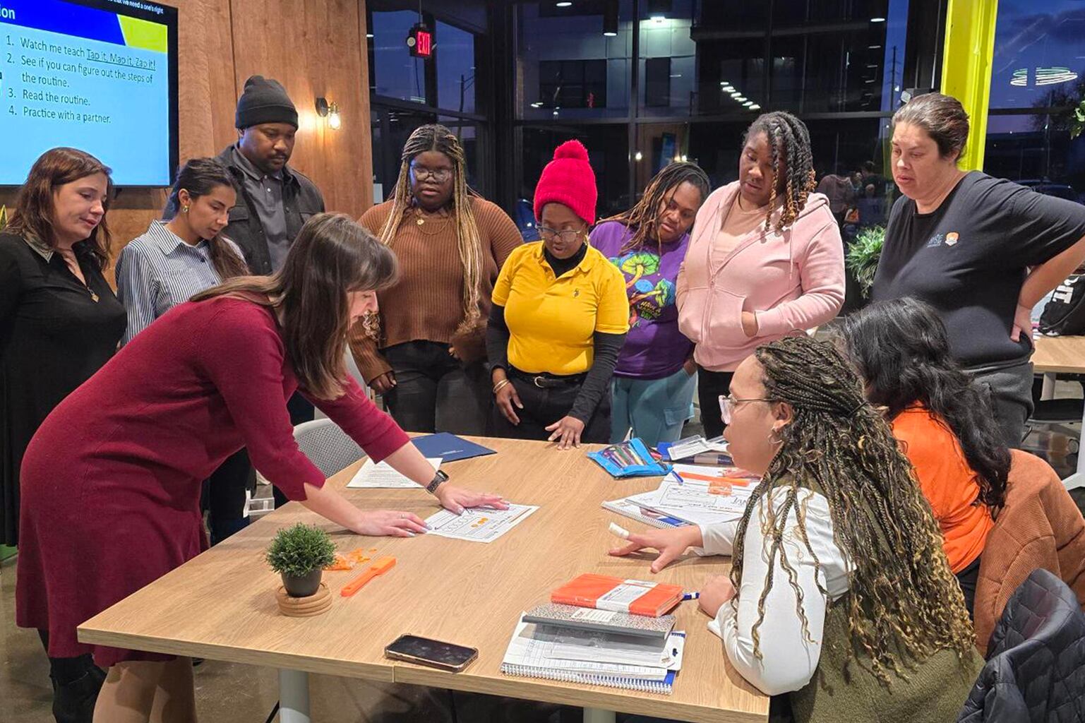A photograph of a large group of people all standing or sitting around a wooden table.
