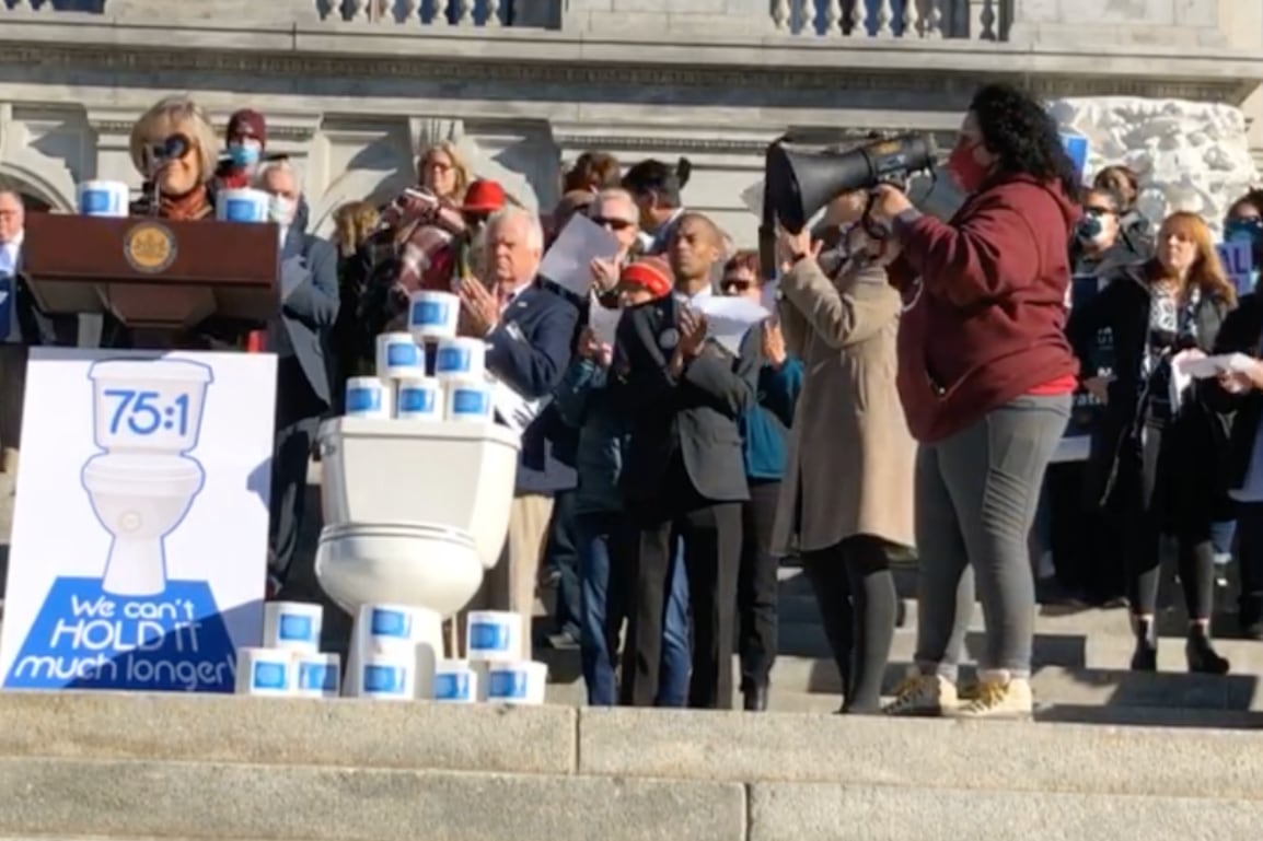 People on the steps of the Pennsylvania Capitol building, with a podium, a toilet and stacks of toilet paper.