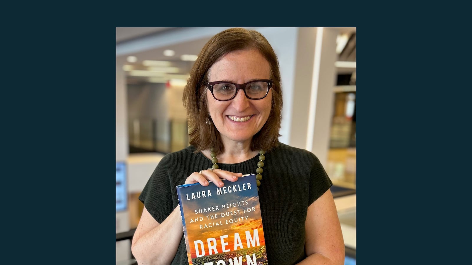A woman with glasses and a black shirt holds a copy of a book