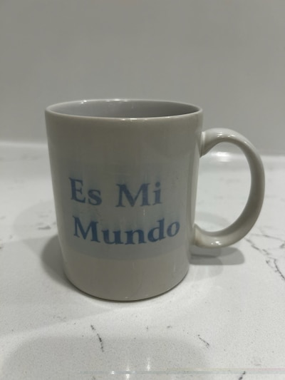 Photograph of a white mug with blue lettering. It reads, "Es Mi Mundo."