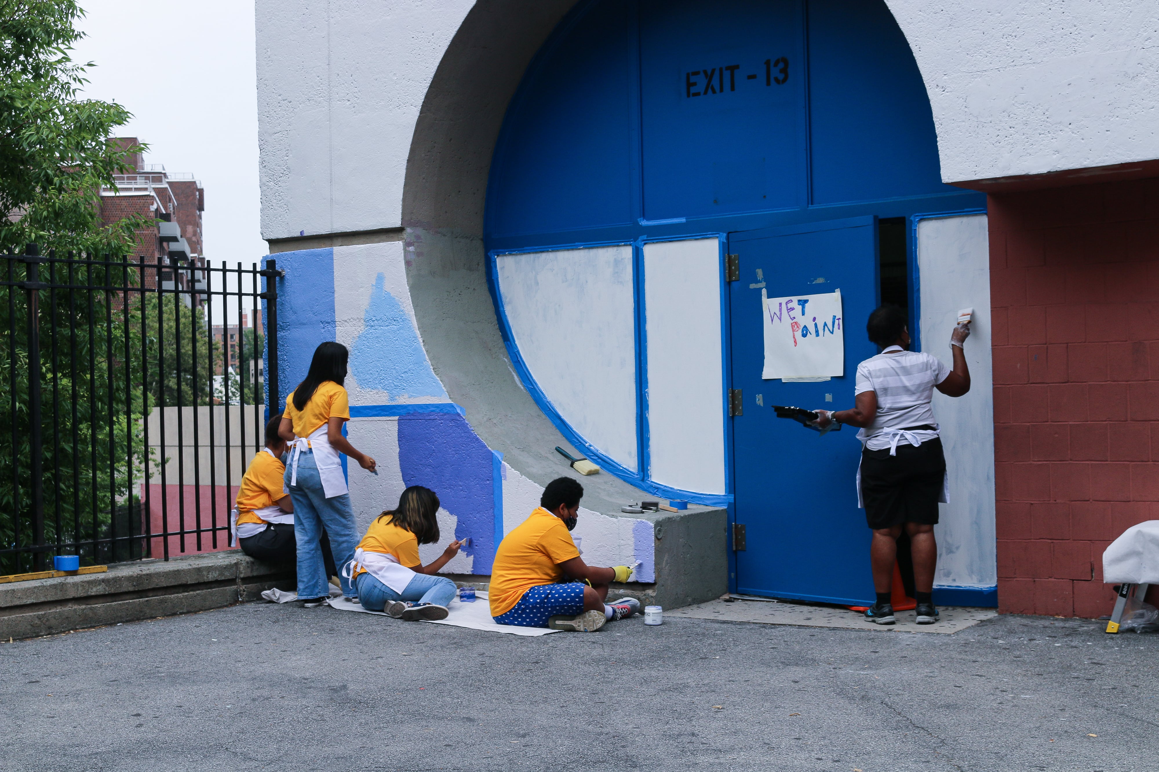 Five people face a wall painting a mural.