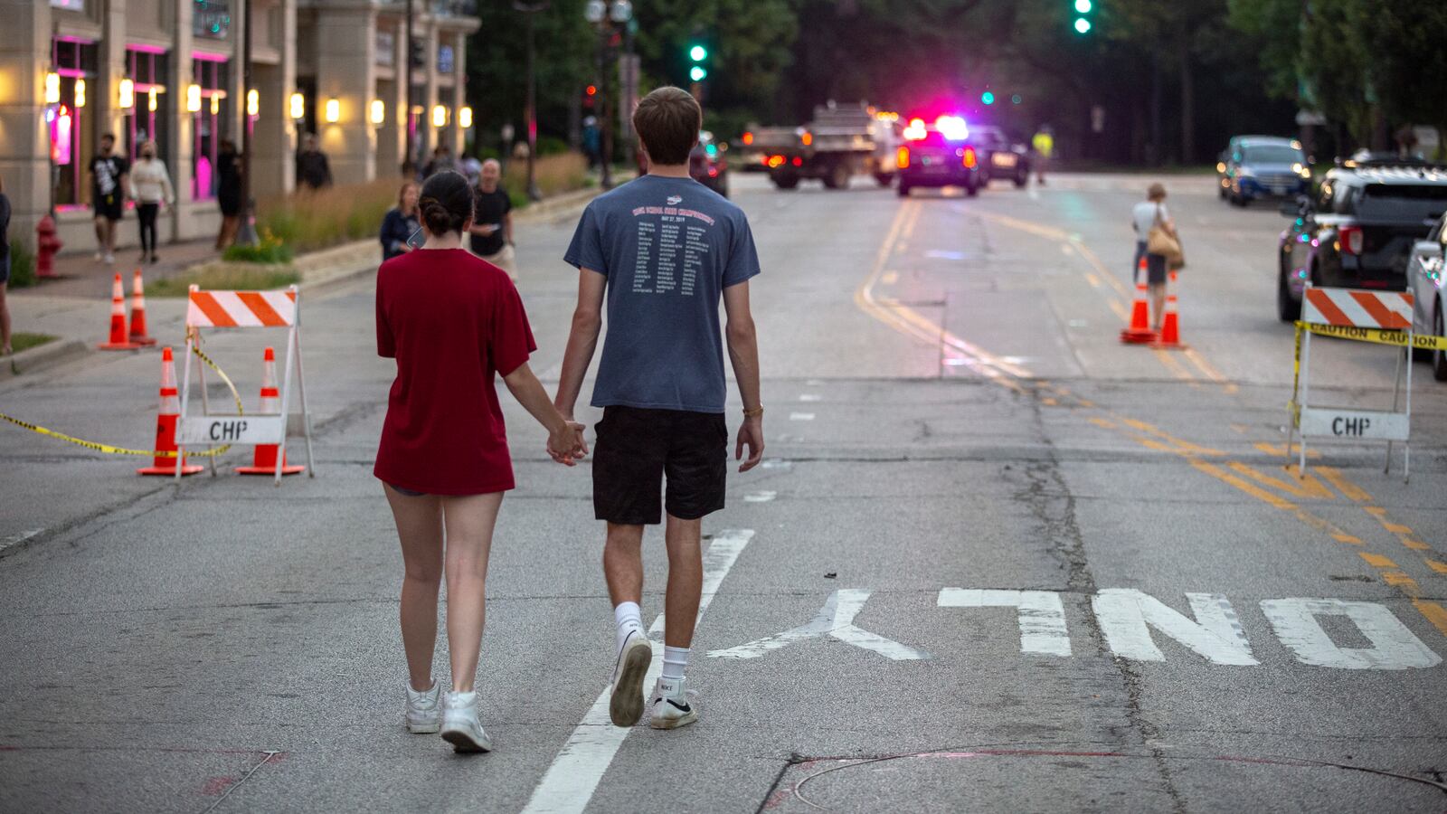 A young couple holding hands walk down the middle of the street in Highland Park, Ill., the road shut down following a mass shooting.