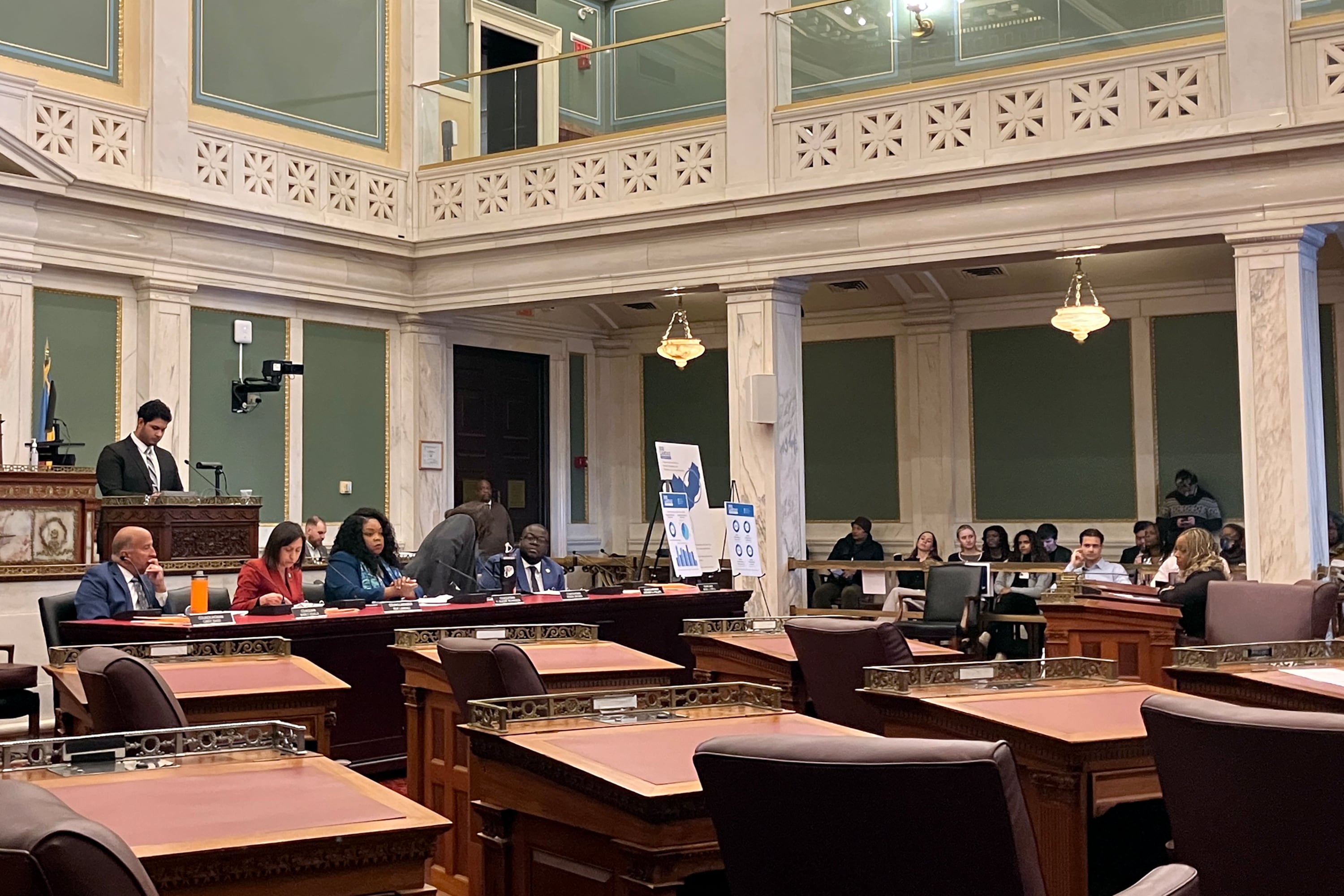 A group of people sit in a large meeting hall in a government building.