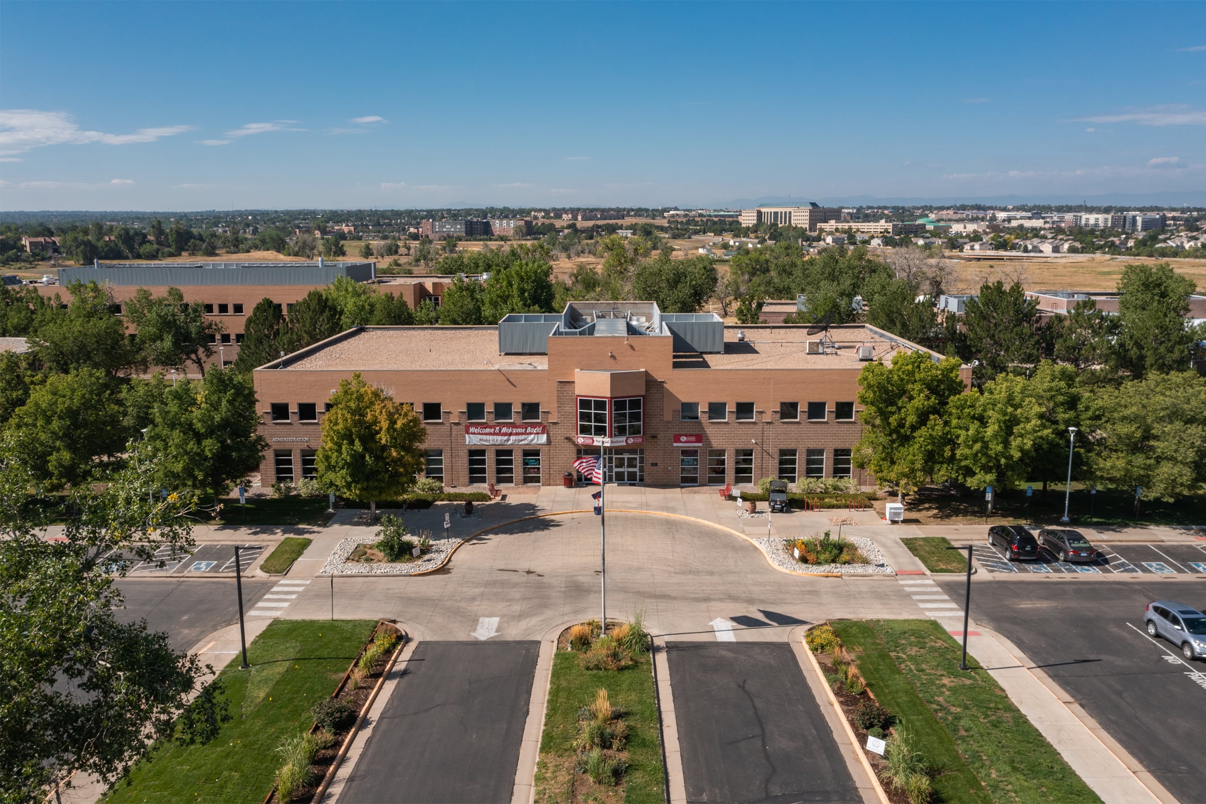 An aerial photo of a brown brick community college campus building with black asphalt roads in front.