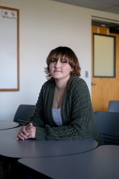 A woman with a gray sweater sits at a table and looks at the camera.