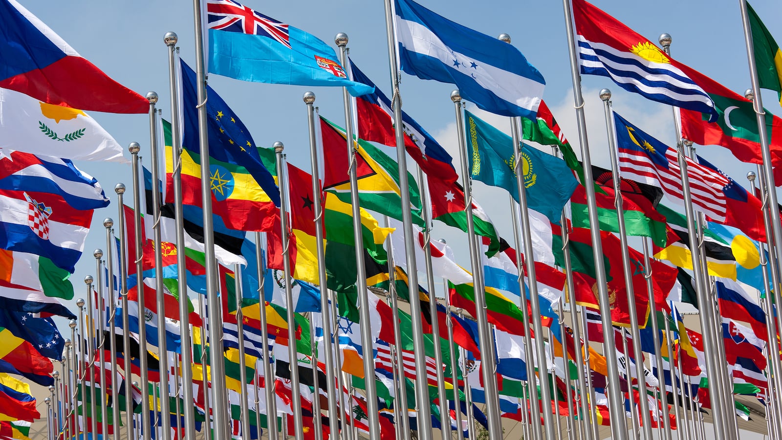 Many national flags on flagpoles with a blue sky in the background.