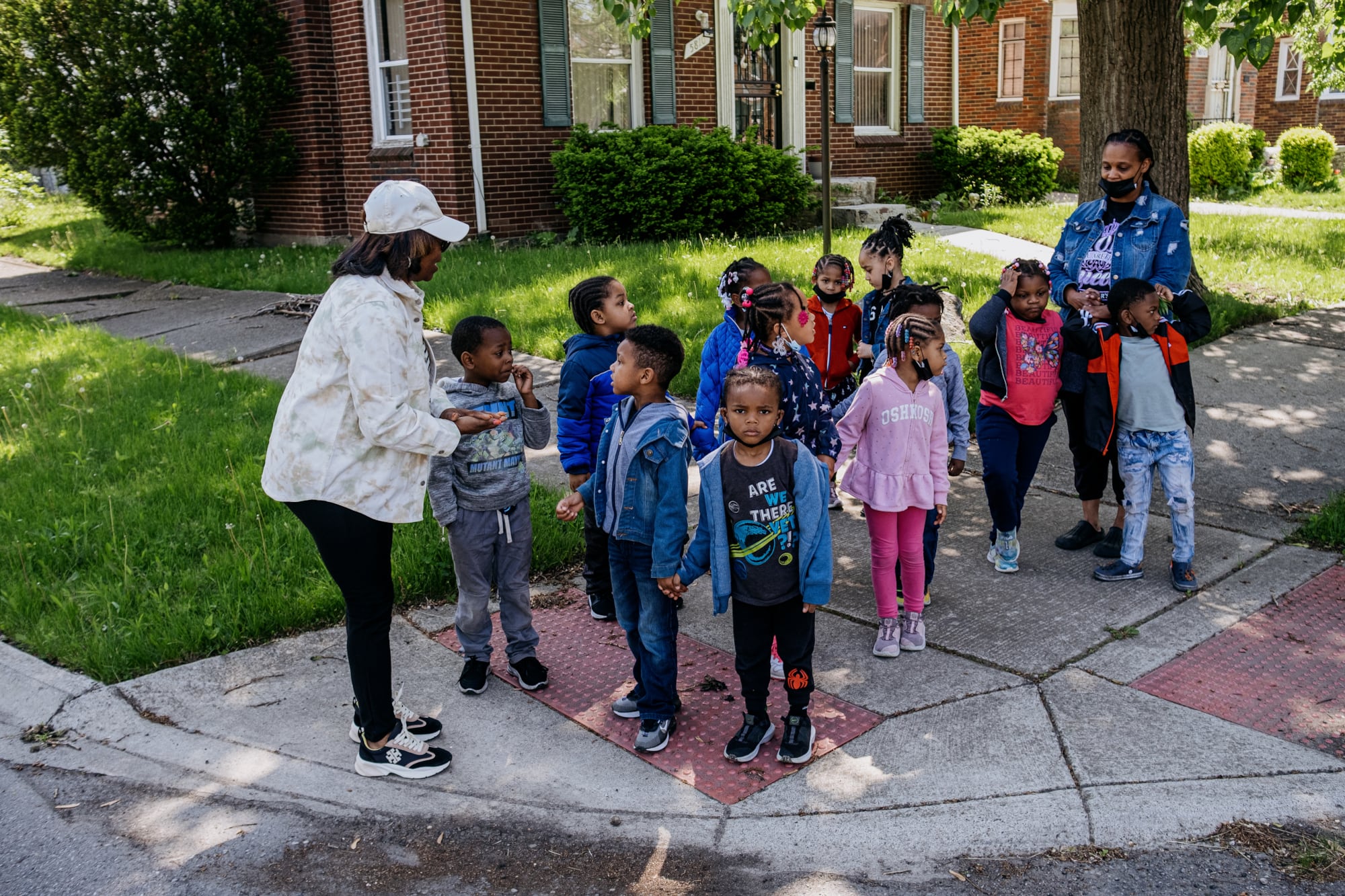 A photograph of a large group of young children and two adults standing at a crosswalk waiting to cross the stree.
