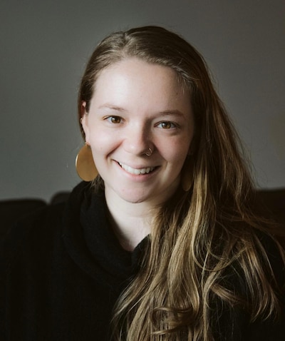 Headshot of a woman with long, light brown hair wearing a black top and gold circular earrings.