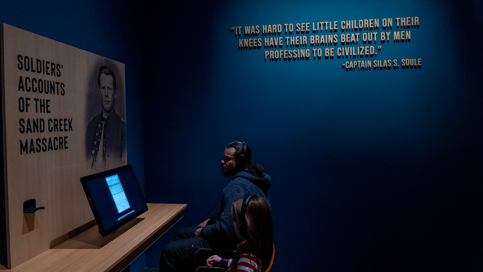 A man and a child look at computer screens at a History Colorado museum exhibit in Denver on the Sand Creek massacre.