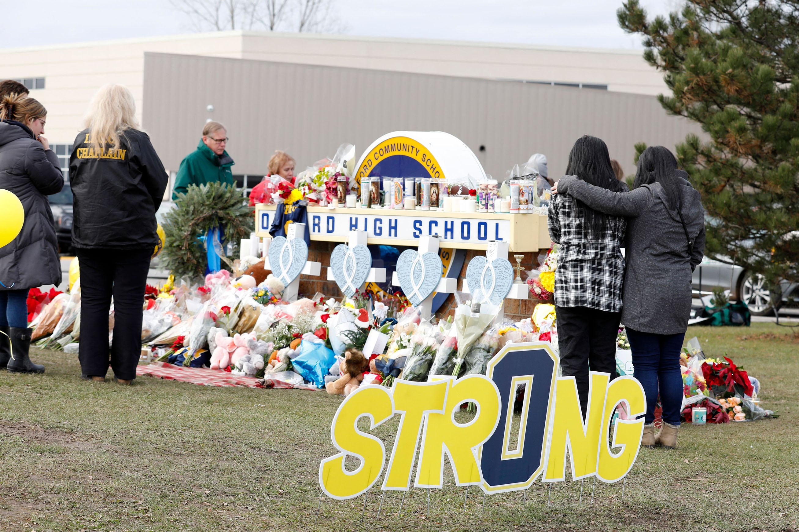 A small group of people stand in front of a memorial in front of Oxford High School outside.