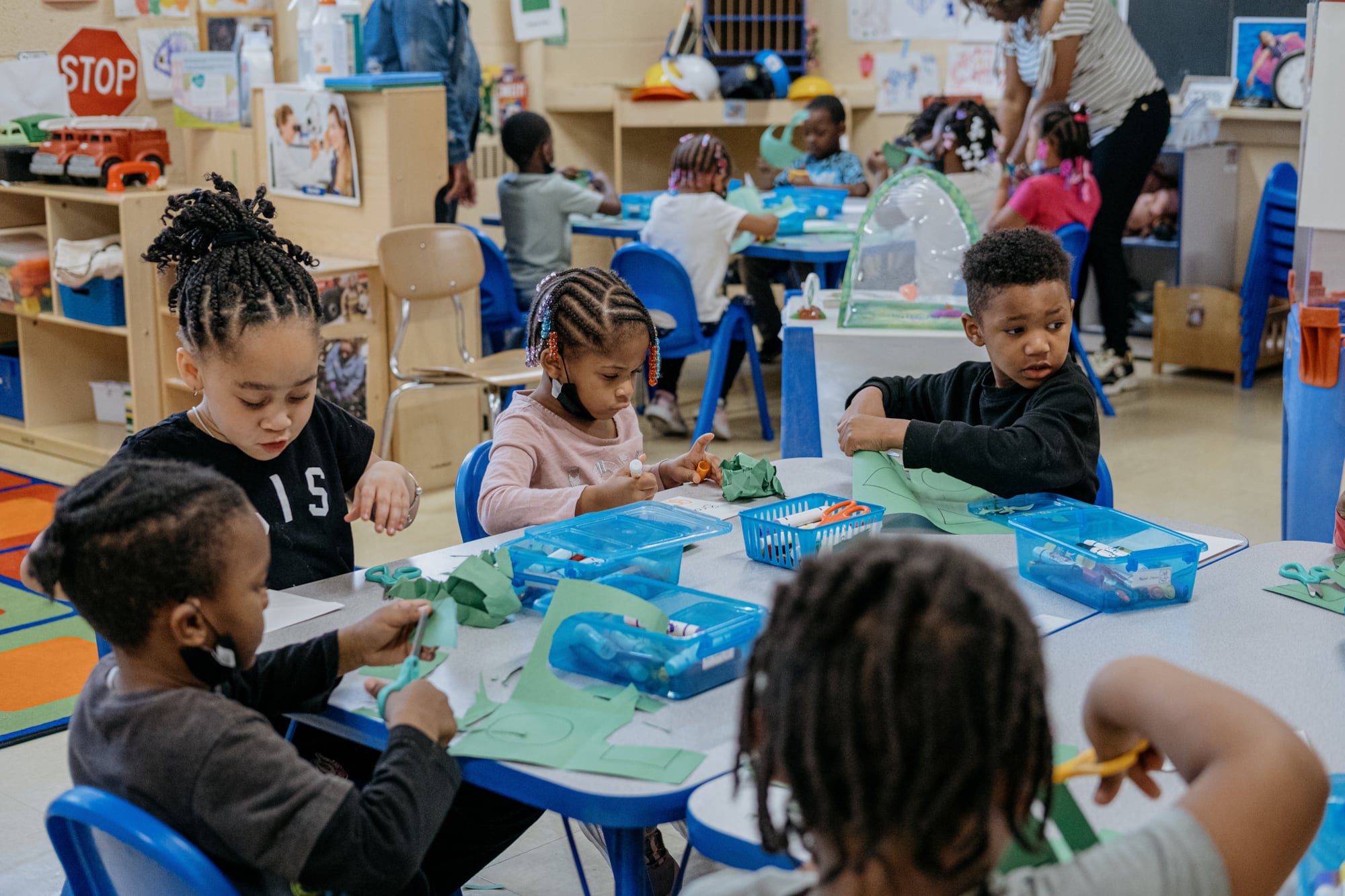 Five students sit focused at a classroom table and use scissors to cut pieces of paper