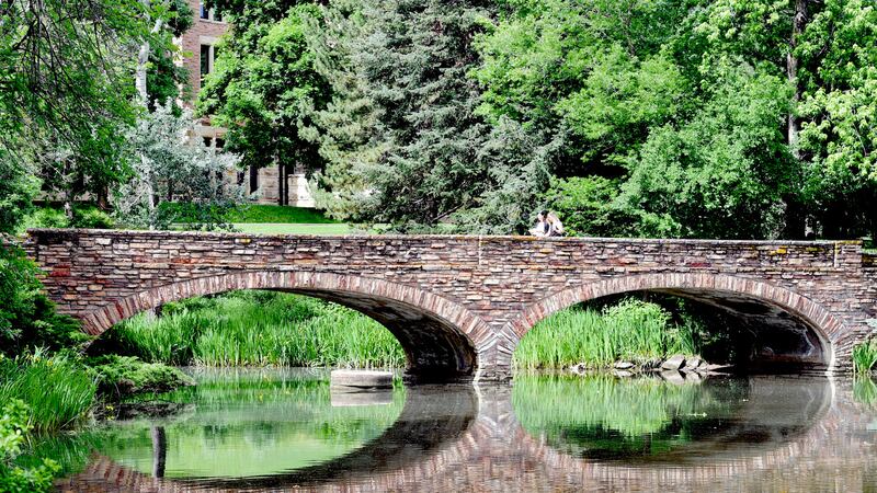 Two women cross the bridge over Varsity Pond on the University of Colorado Boulder campus on June 27, 2019.
