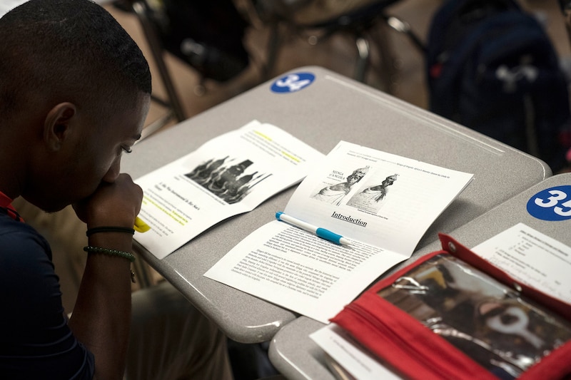 A view from behind and above of a young student who is reading at a desk in a classroom.