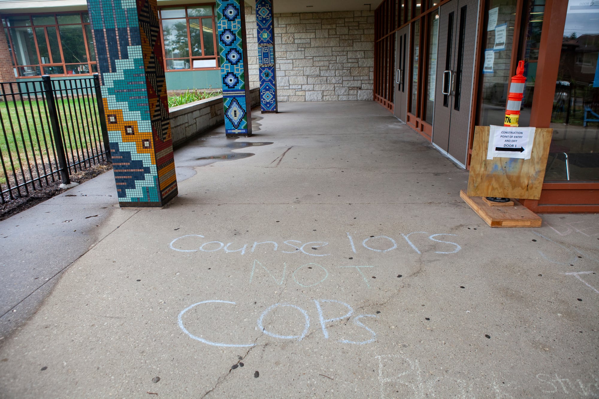 Chalk on the sidewalk outside of the school reads Counselors not cops.