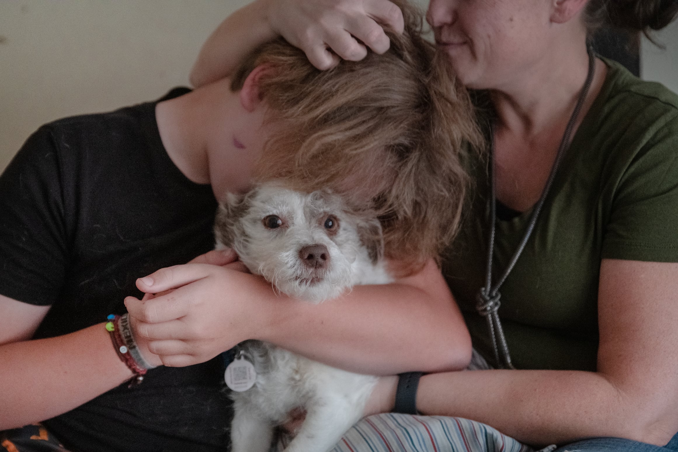 A woman hugs her 13-year-old son’s head. Her face and his face are obscured. The boy is hugging a small white dog.
