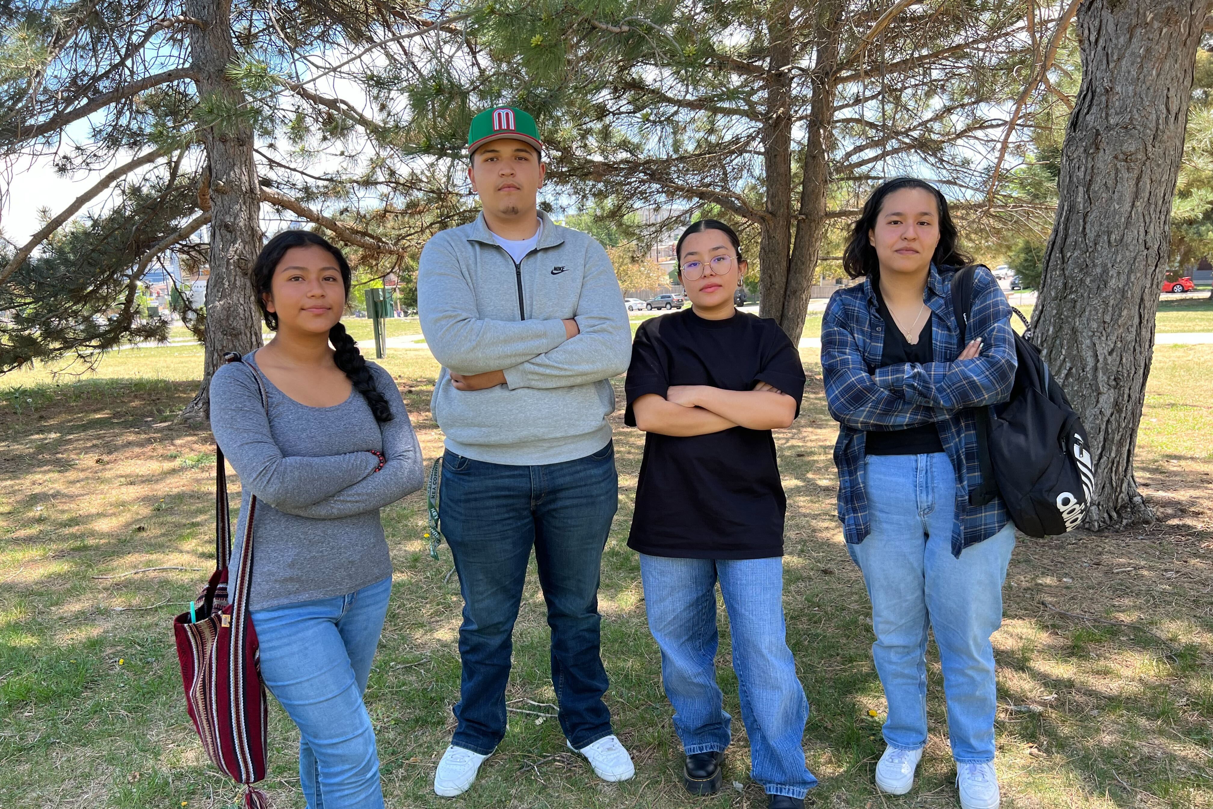 Four high school students pose in a park. They stand with their arms crossed.