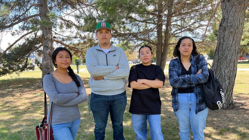 Four high school students pose in a park. They stand with their arms crossed.
