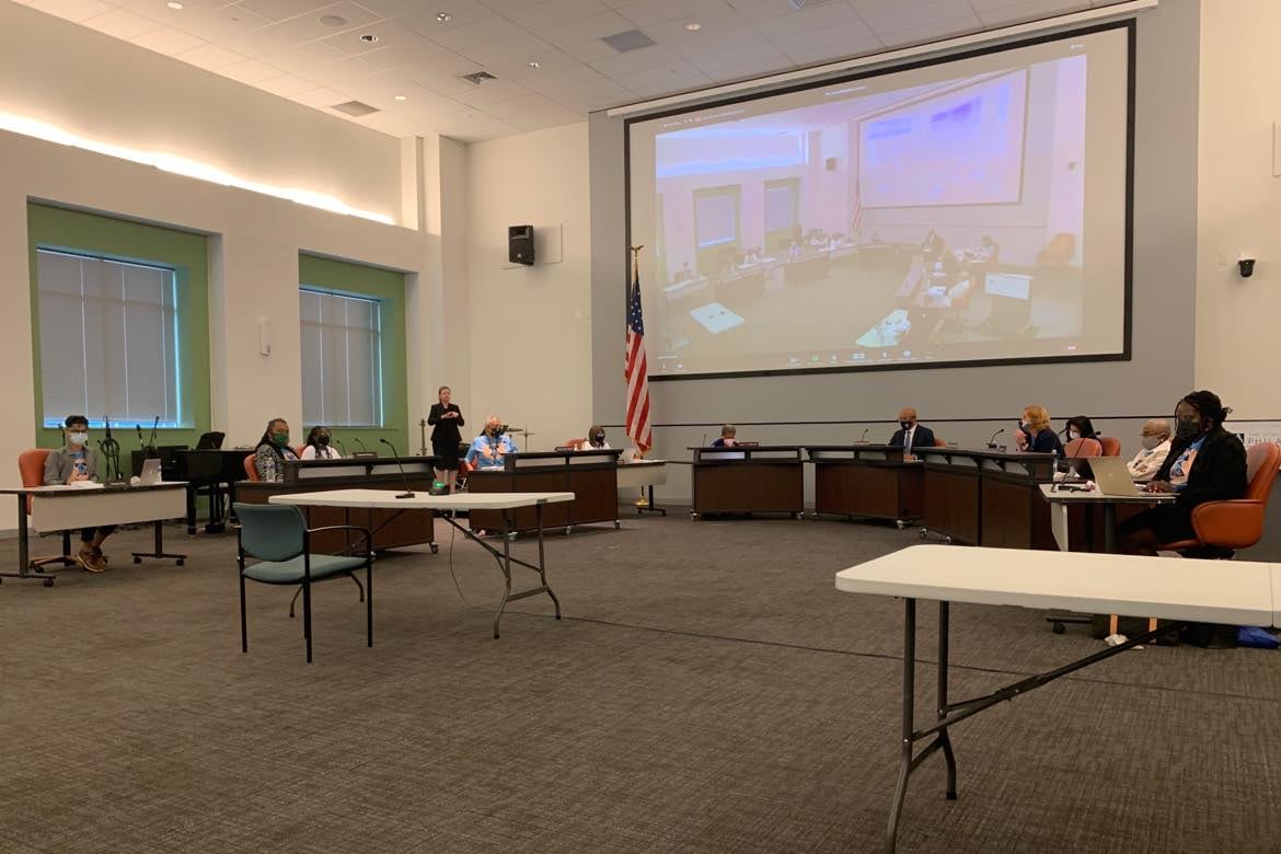 Board of Education meeting inside the meeting hall of the School District of Philadelphia’s headquarters. Participants are socially distanced and the foreground shows a lot of empty carpeted area.