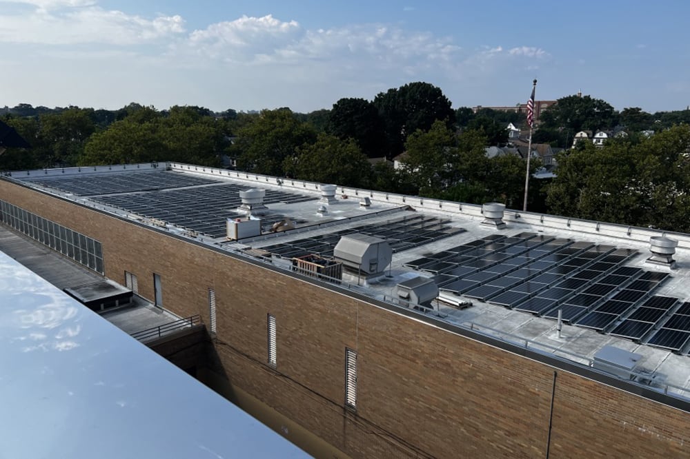 A photograph of solar panels on top of a brick building with trees in the background.