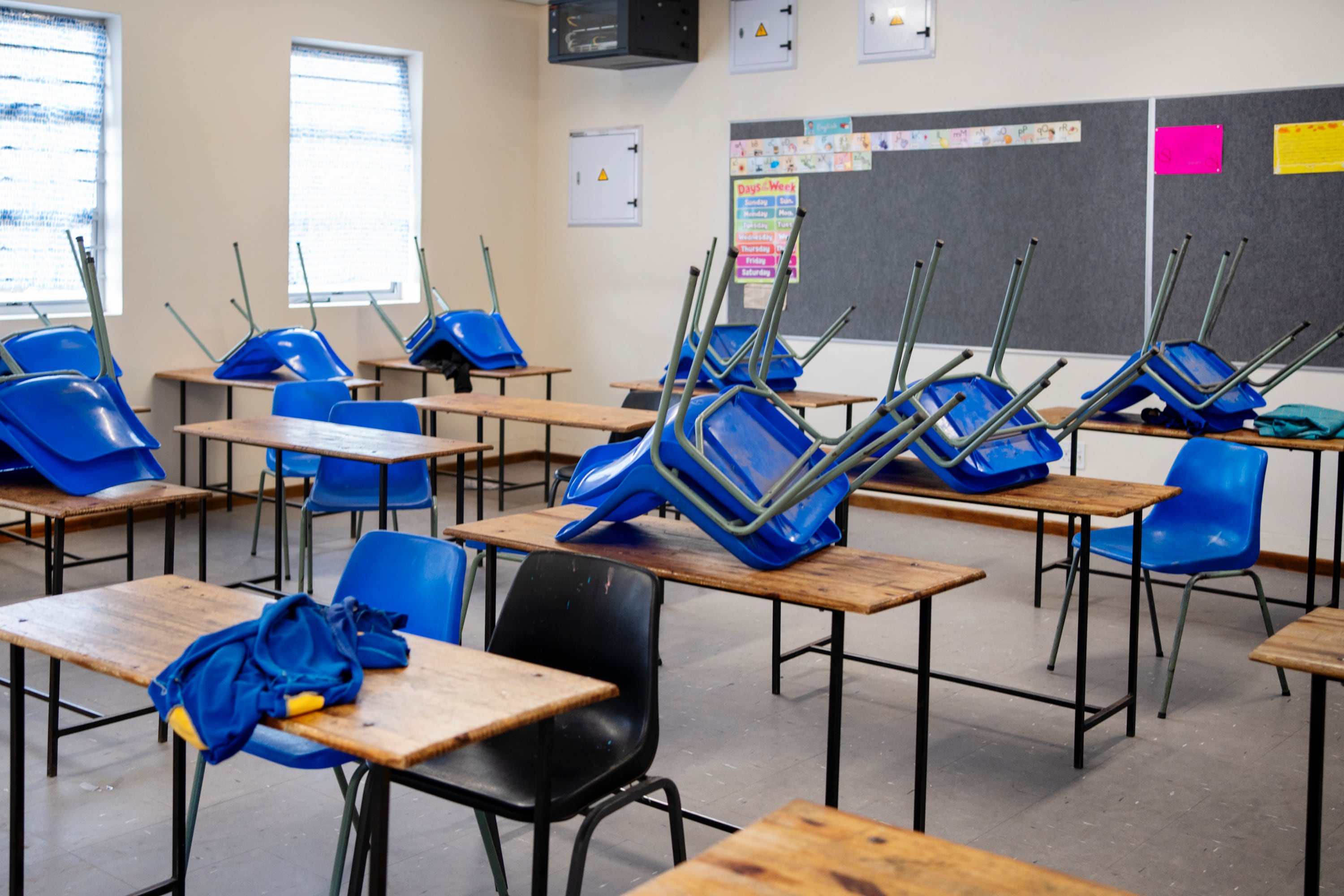 A photograph of an empty classroom with blue chairs stacked on top of wooden tables.