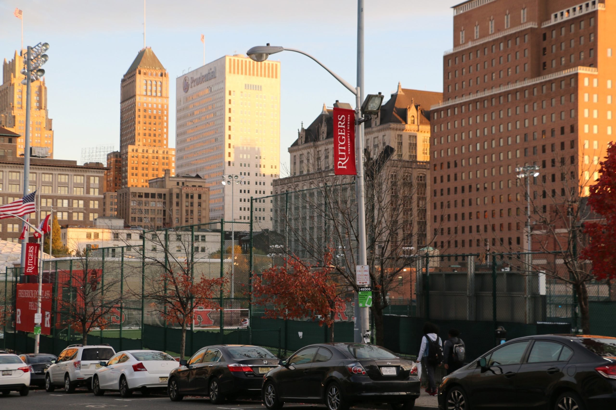 A photograph of the Newark campus of Rutgers University, with golden light reflecting against large buildings in the background.