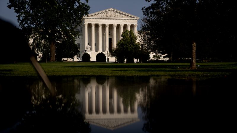 The United States Supreme Court building is reflected in a pool of water as it stands in the background of the image.