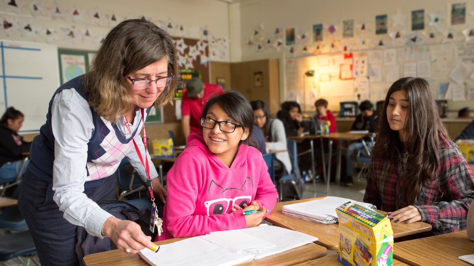 A teacher stands behind a student assisting them with classwork.