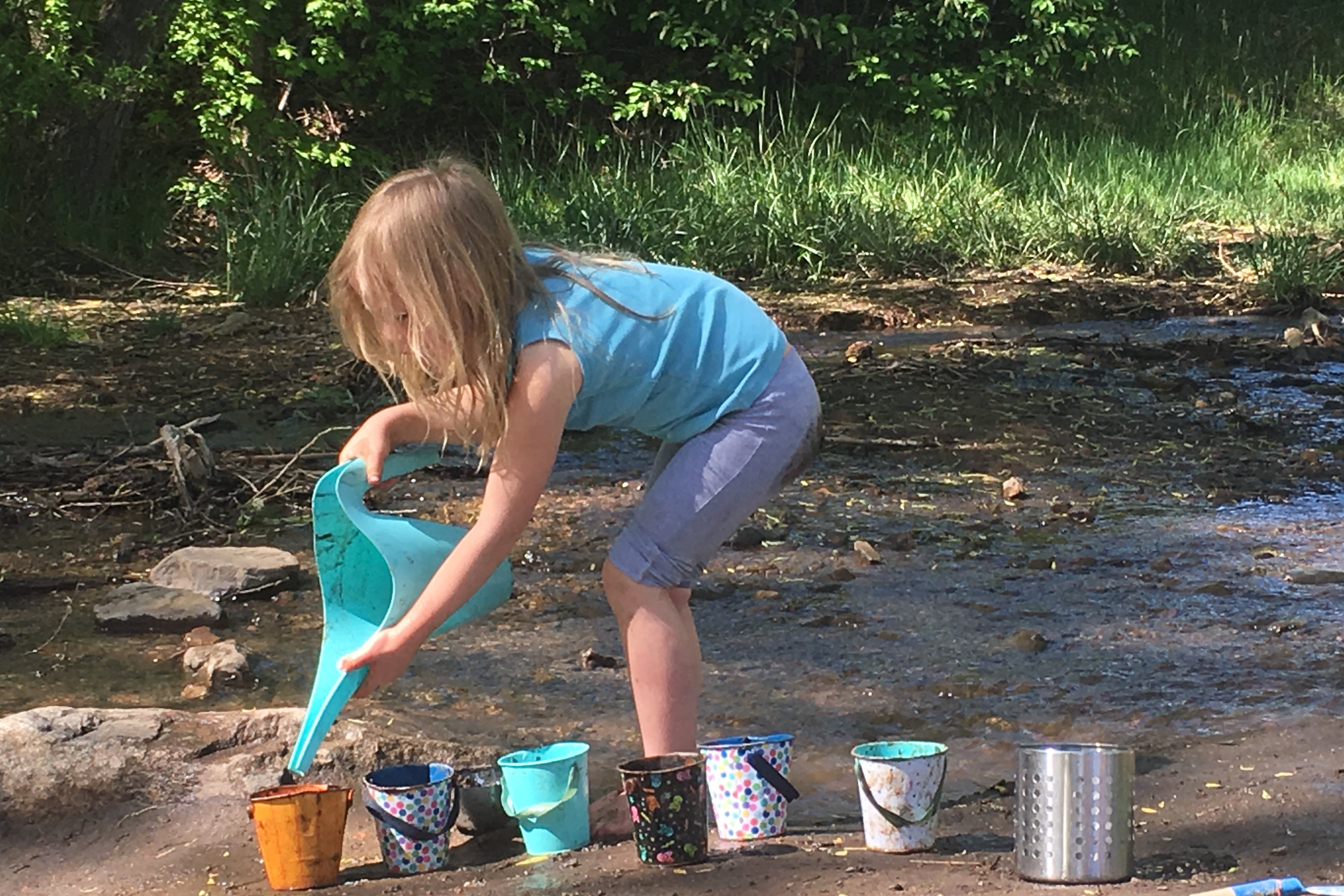 A girl in blue pours water from a blue container.