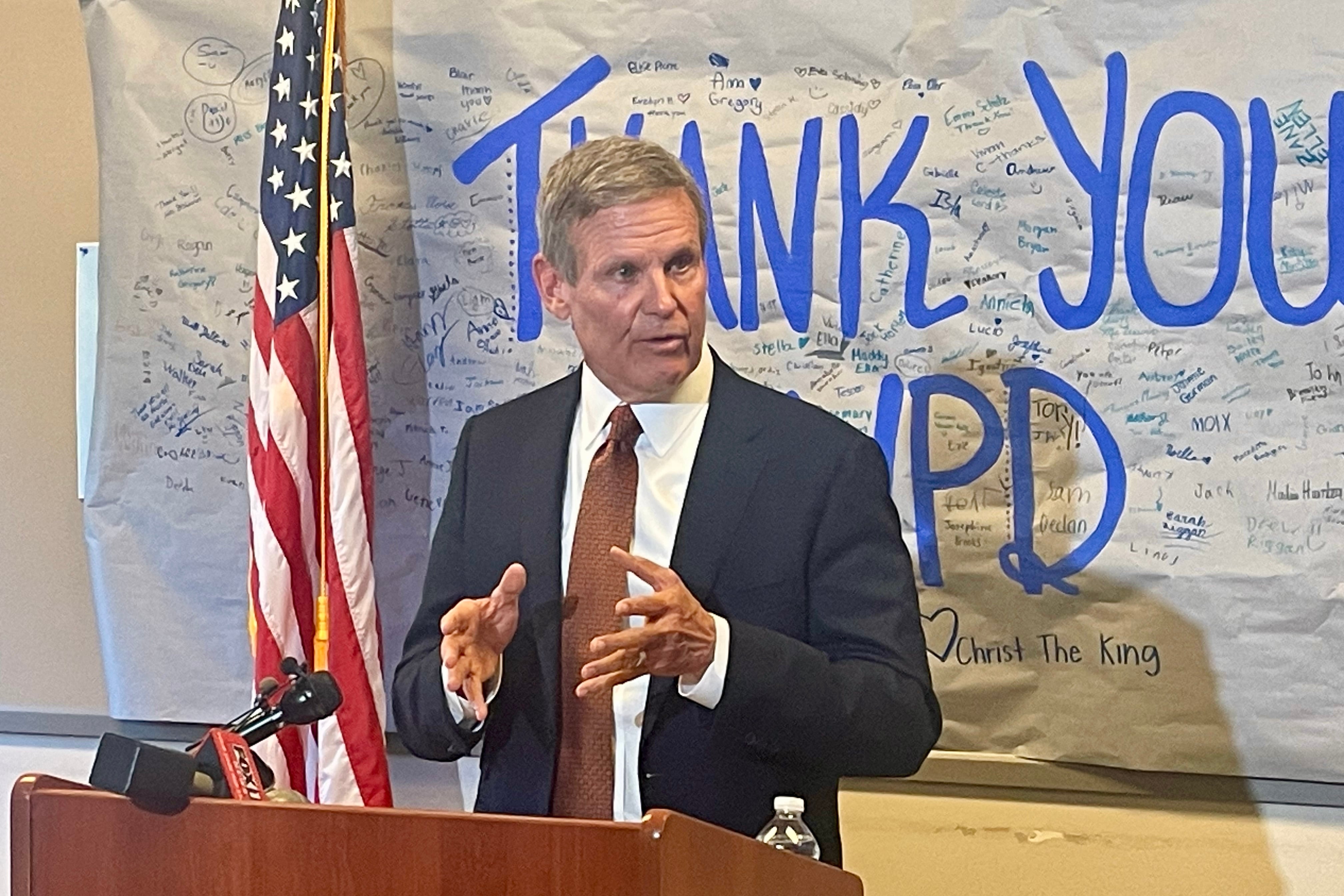 A man in a business suit speaks at a podium with the U.S. flag in the background.