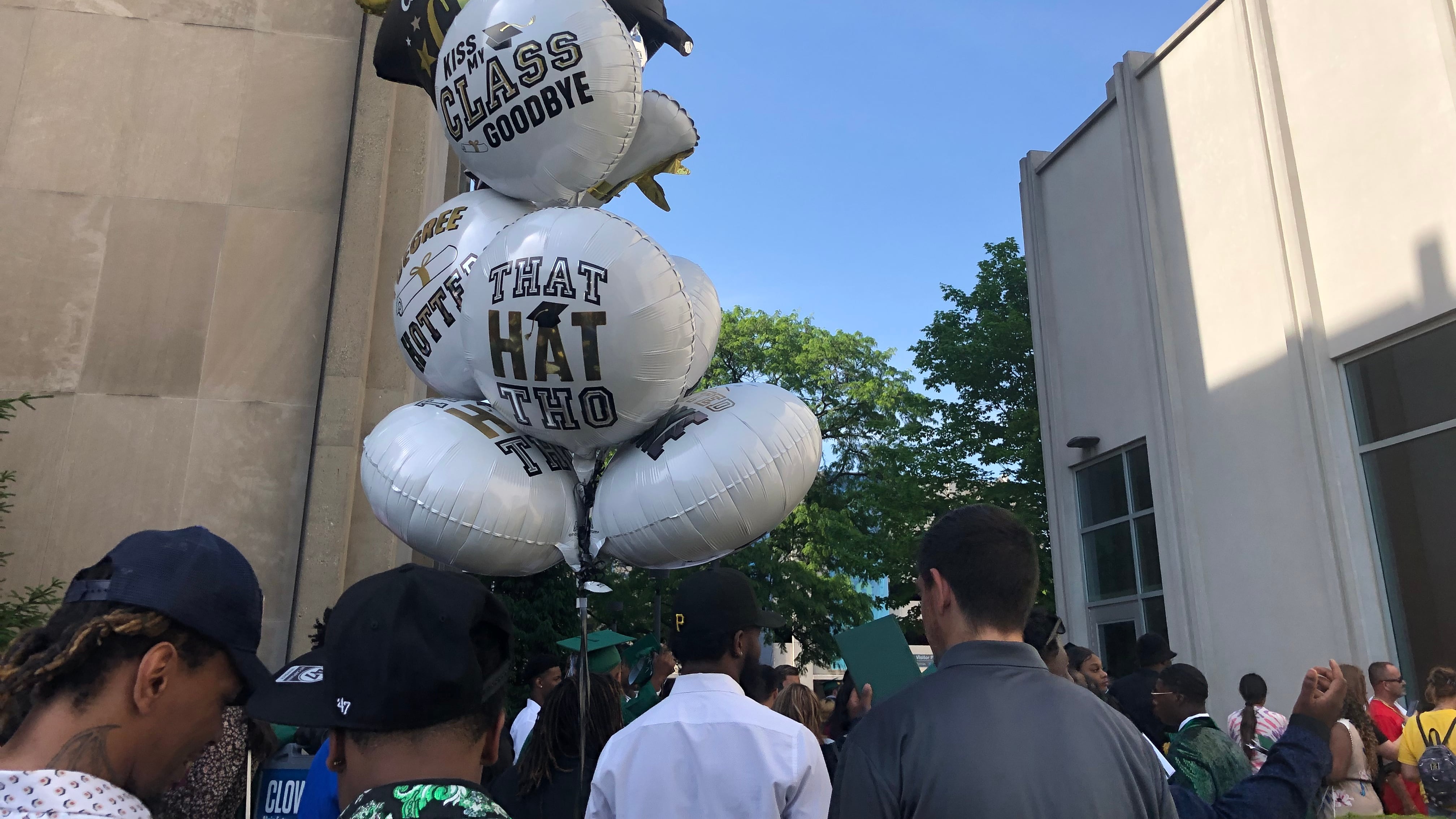 Family members of high school graduates hold celebratory balloons outside of a large memorial hall.