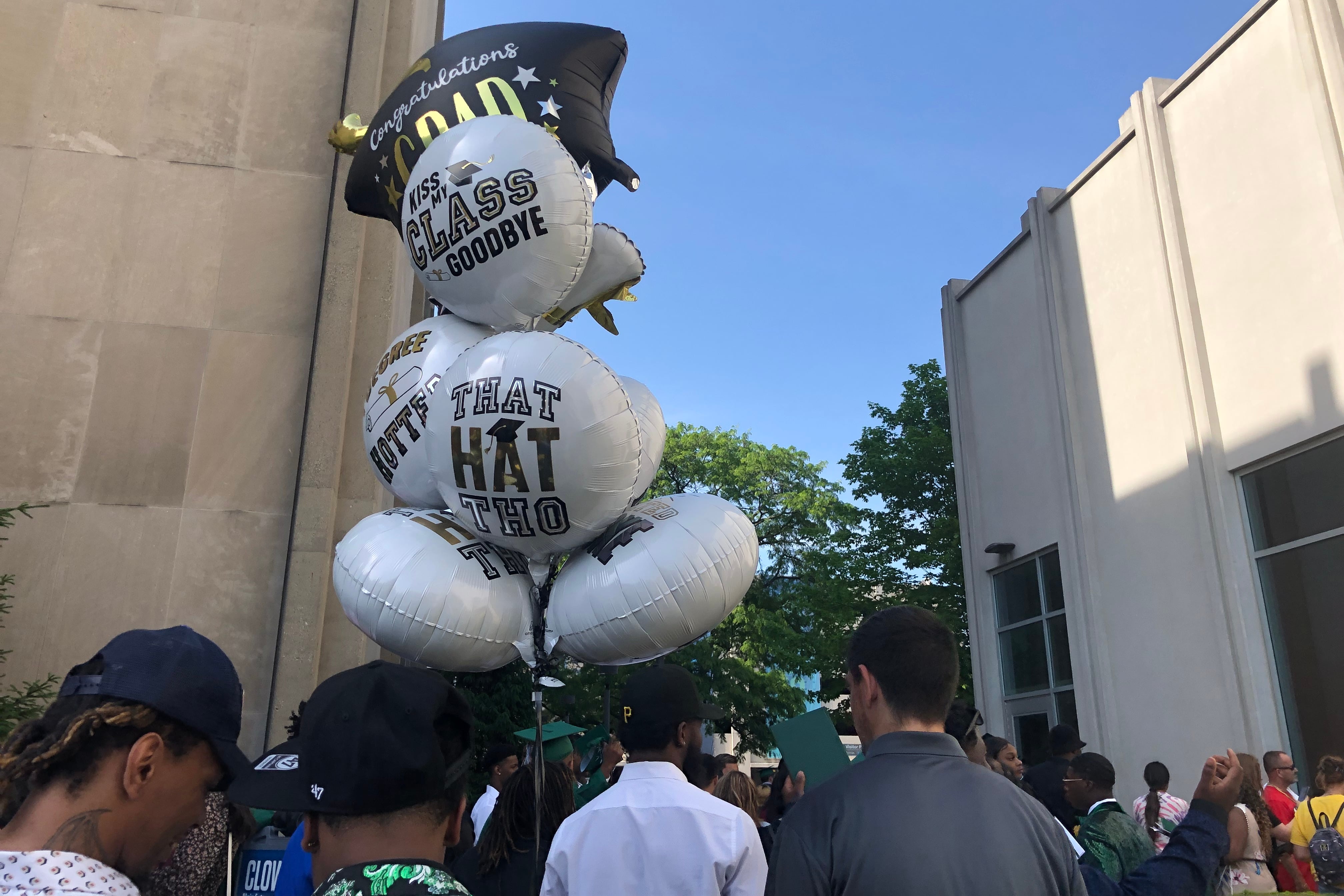 Family members of high school graduates hold celebratory balloons outside of a large memorial hall.
