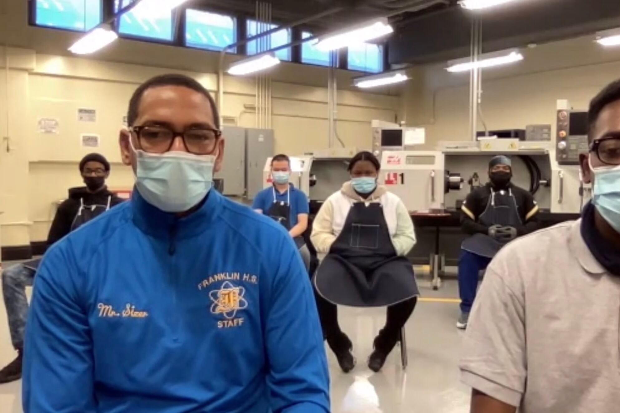 Teacher Ronald Sizer sits next to student Warren Crosby with other students and machines behind them.