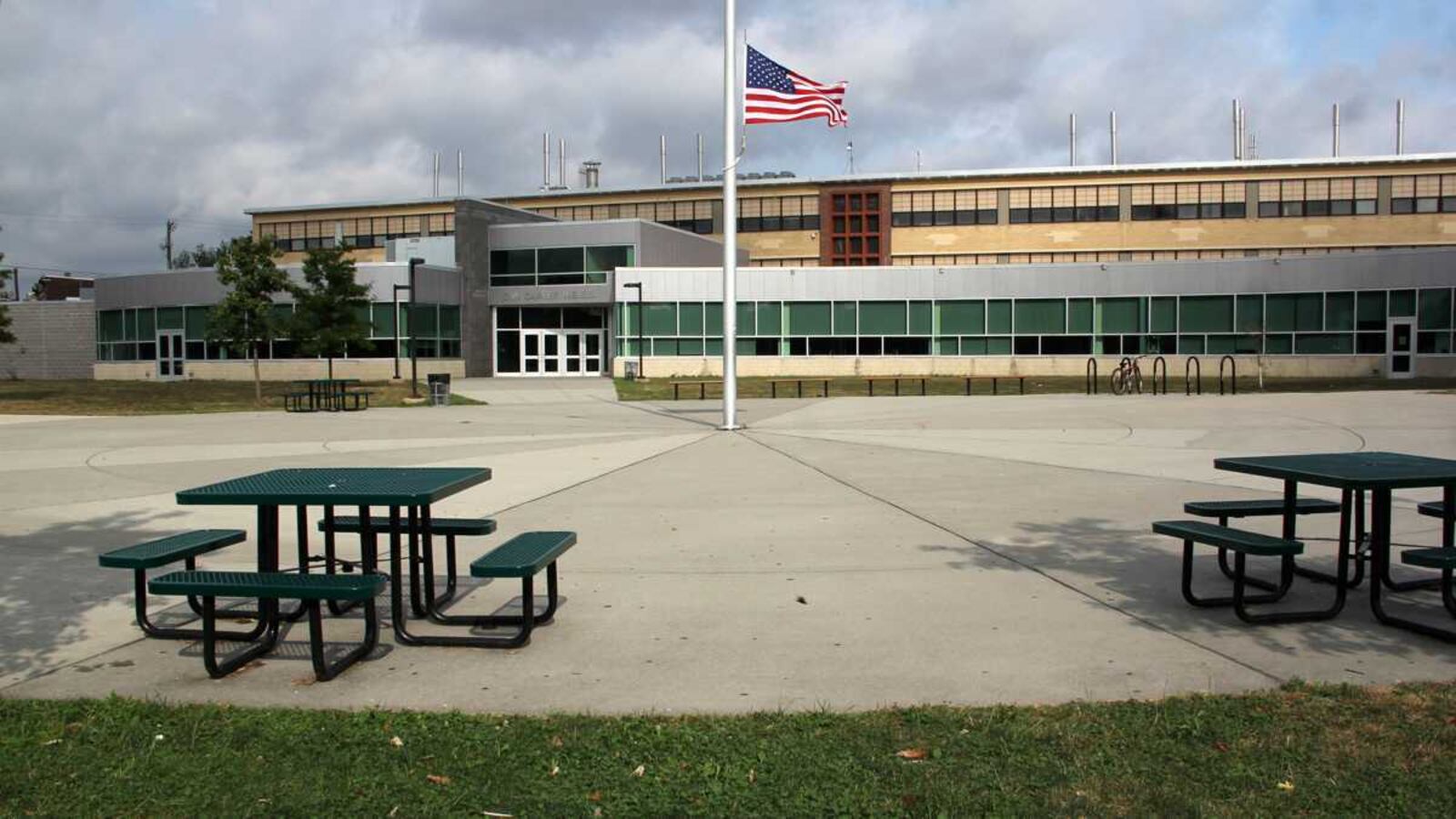The exterior of Carver High School in Philadelphia, with small picnic tables in the foreground and a U.S. flag flying on a flagpole.