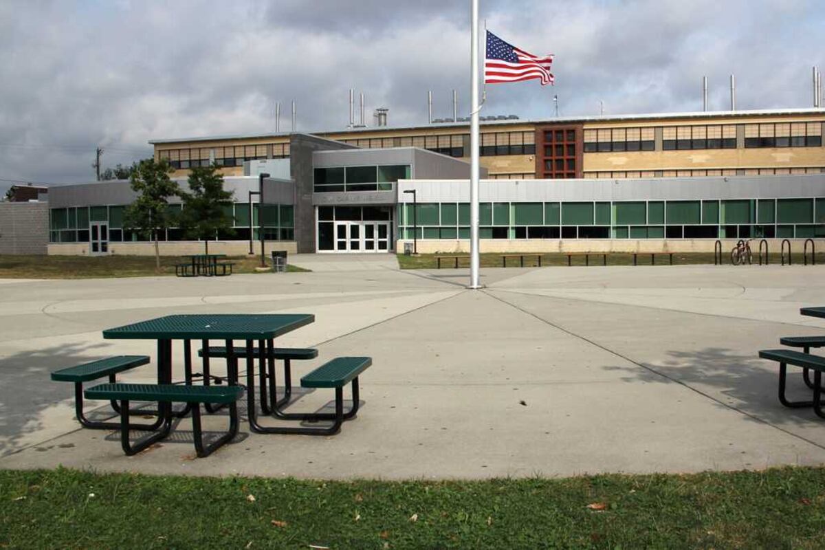 The exterior of Carver High School in Philadelphia, with small picnic tables in the foreground and a U.S. flag flying on a flagpole.